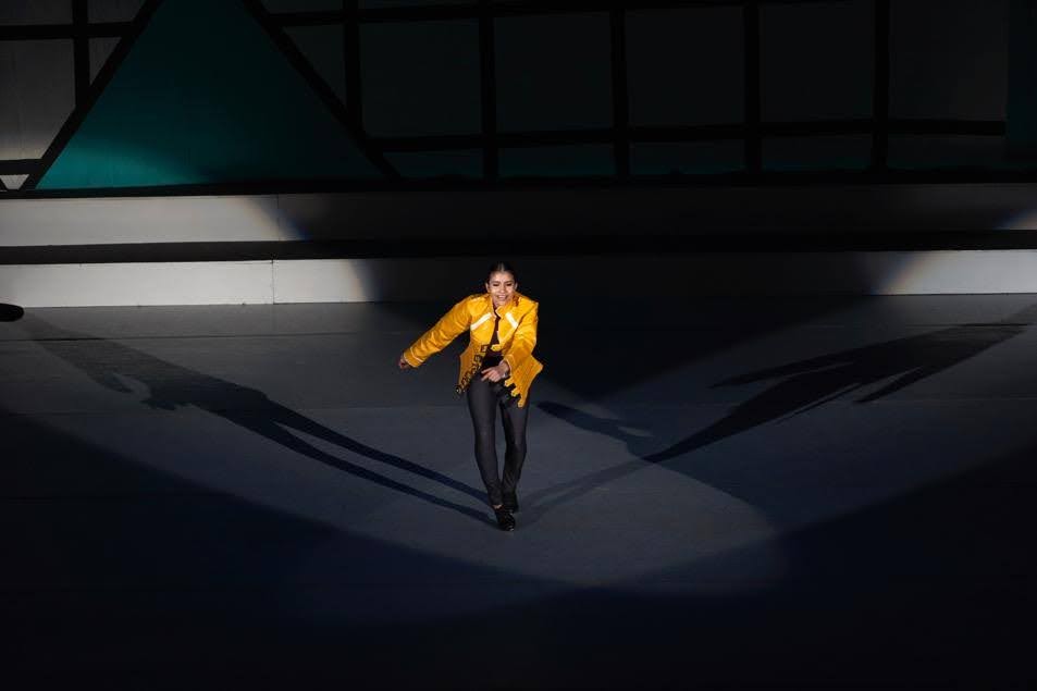 Anneth Paola Davis dancing in a yellow jacket under a stage spotlight